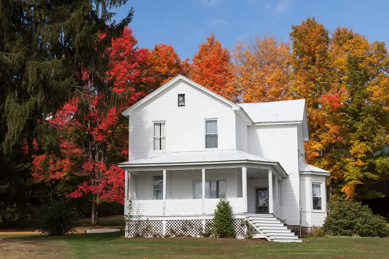 Old white house with steps leading up to porch and bay window, surrounded by beautiful fall foliage