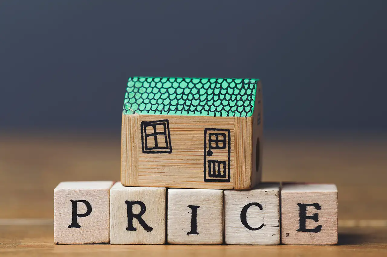 Wooden building block house with green roof sitting on top of letter blocks spelling