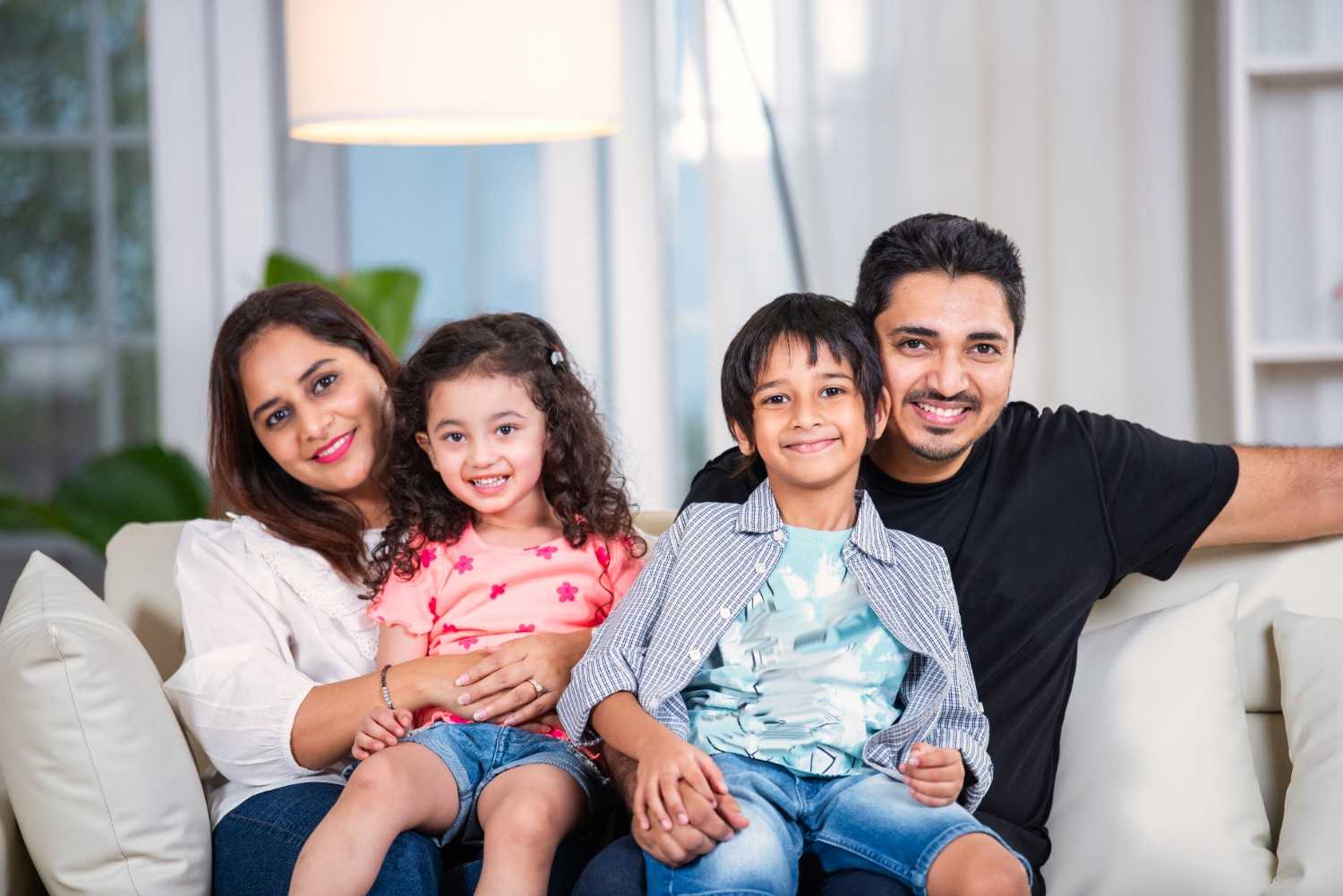 A happy family portrait of parents and children smiling together on a couch in their Aberdeen, MD home