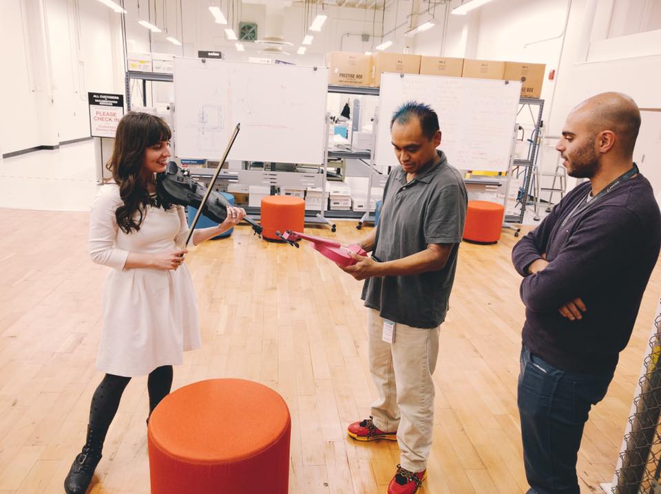 Kaitlyn Hova playing violin while two NASA employees look at another Hovalin