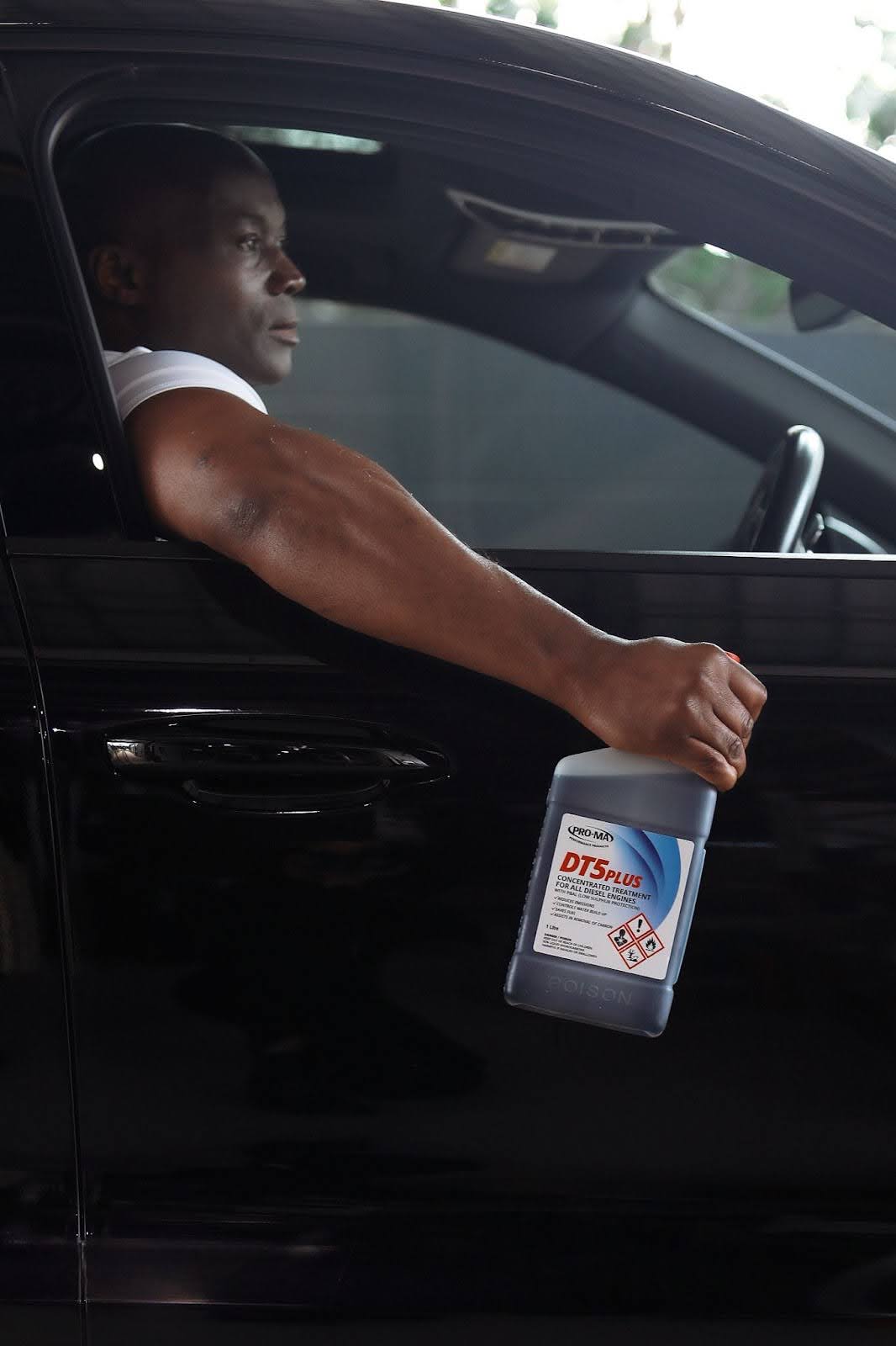 Man sitting in driver seat of black car holding a bottle of DT5 out of the window.