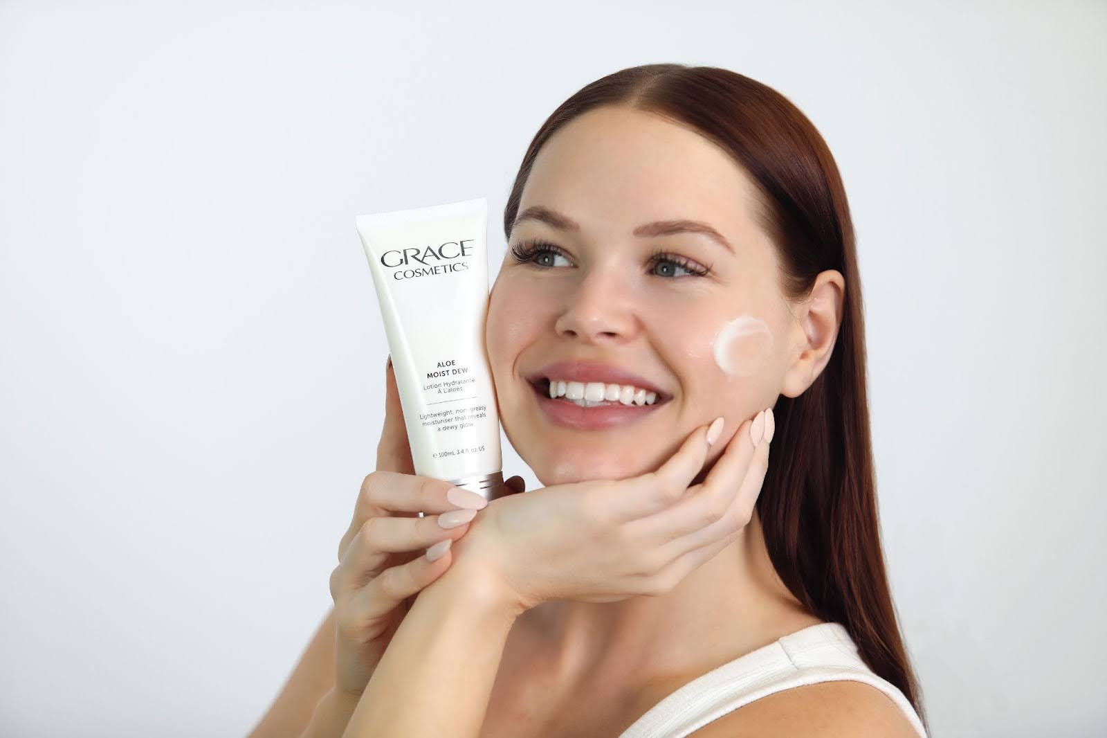 Close up of young woman holding a Grace Cosmetics product by her cheek