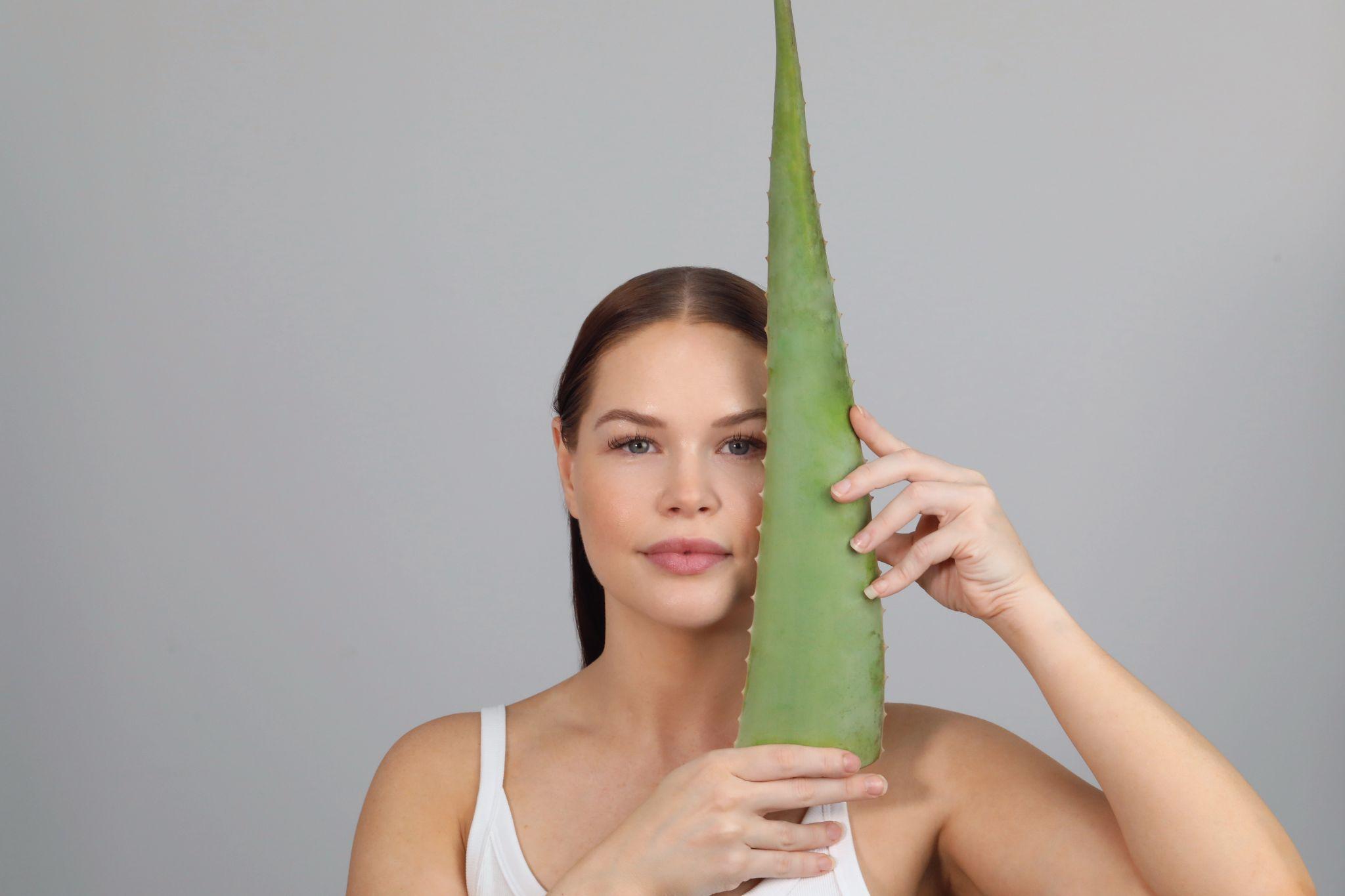 Woman holding a fresh aloe vera leaf beside her face