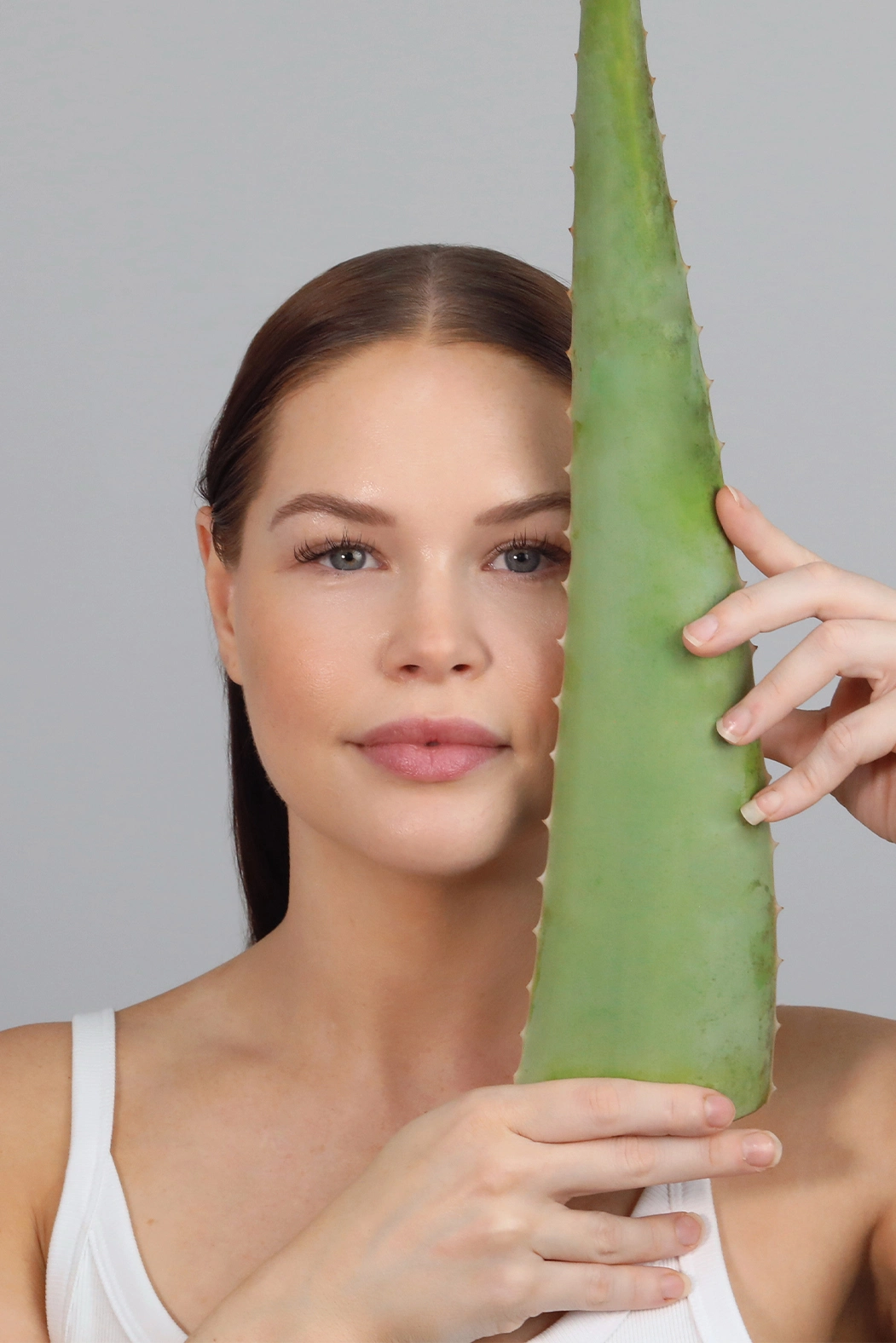 Woman holding a fresh aloe vera leaf beside her face