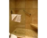 walk-in frameless shower tiled in travetine and beach pebble accents
