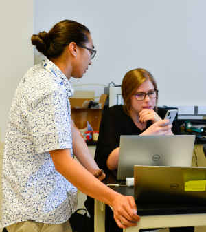 Two CU students, one male and one female, discuss their test using a mobile device. 