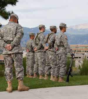 Four US Army soldiers and their commander stand at attention to the US flag on the University of Colorado Colorado Springs campus. 