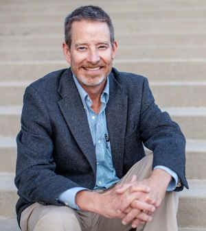 Professor Charles "Chip" Benight sits outside on the stairs smiling