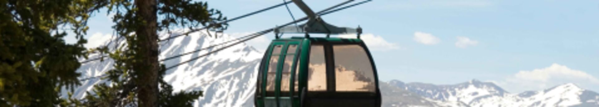 A gondola lift at Keystone Resort, Colorado, suspended in mid-air with a backdrop of snow-capped mountains and evergreen trees under a clear blue sky