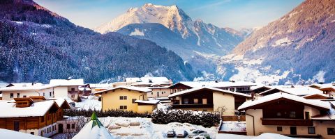 Mayrhofen village surrounded by dense snow-capped forests and mountains in soft evening light