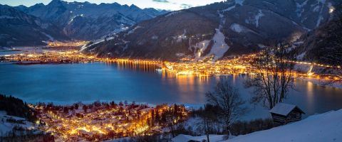 Night view of Zell am See with its lake reflecting the lights from the town and surrounding snowy mountains