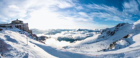 Panoramic view of the revolving restaurant on the snowy peaks of Saas-Fee with clouds below.