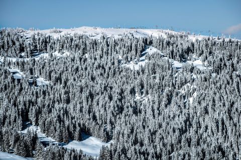 A picturesque snow-covered alpine village with a tall church steeple, backed by dramatic snowy mountain peaks.