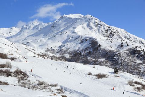 Skiers enjoying the slopes on a wide, groomed piste under bright skies.