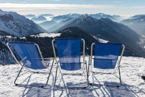 Three blue sun loungers overlooking a snow-covered mountain range in Pinzolo, Italy