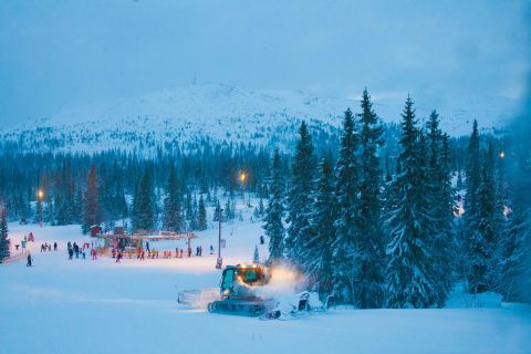 Snow-covered ski resort in Trysil at night with a snow grooming machine and skiers in the background