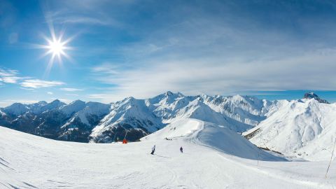 Skiers descending a wide piste under a blue sky