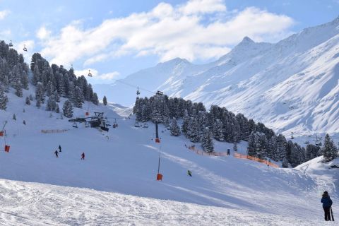 Ski resort in Austria with skiers descending a wide piste under a blue sky