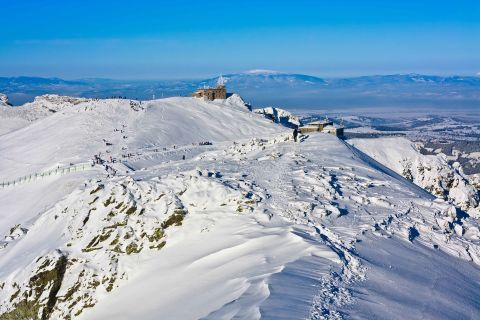 Snow-covered ridge and summit buildings at Kasprowy Wierch ski resort in Poland, with distant views of the valley and mountains under a clear blue sky