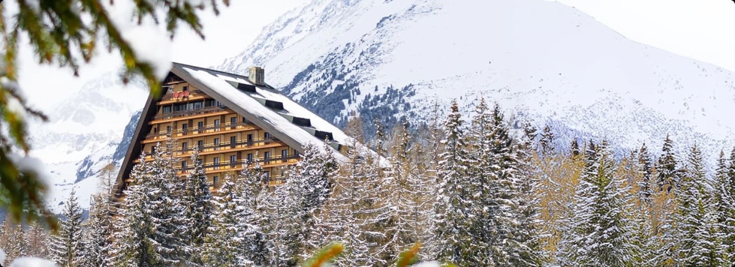 Ski chalet hotel framed by snow-covered pines with mountains behind