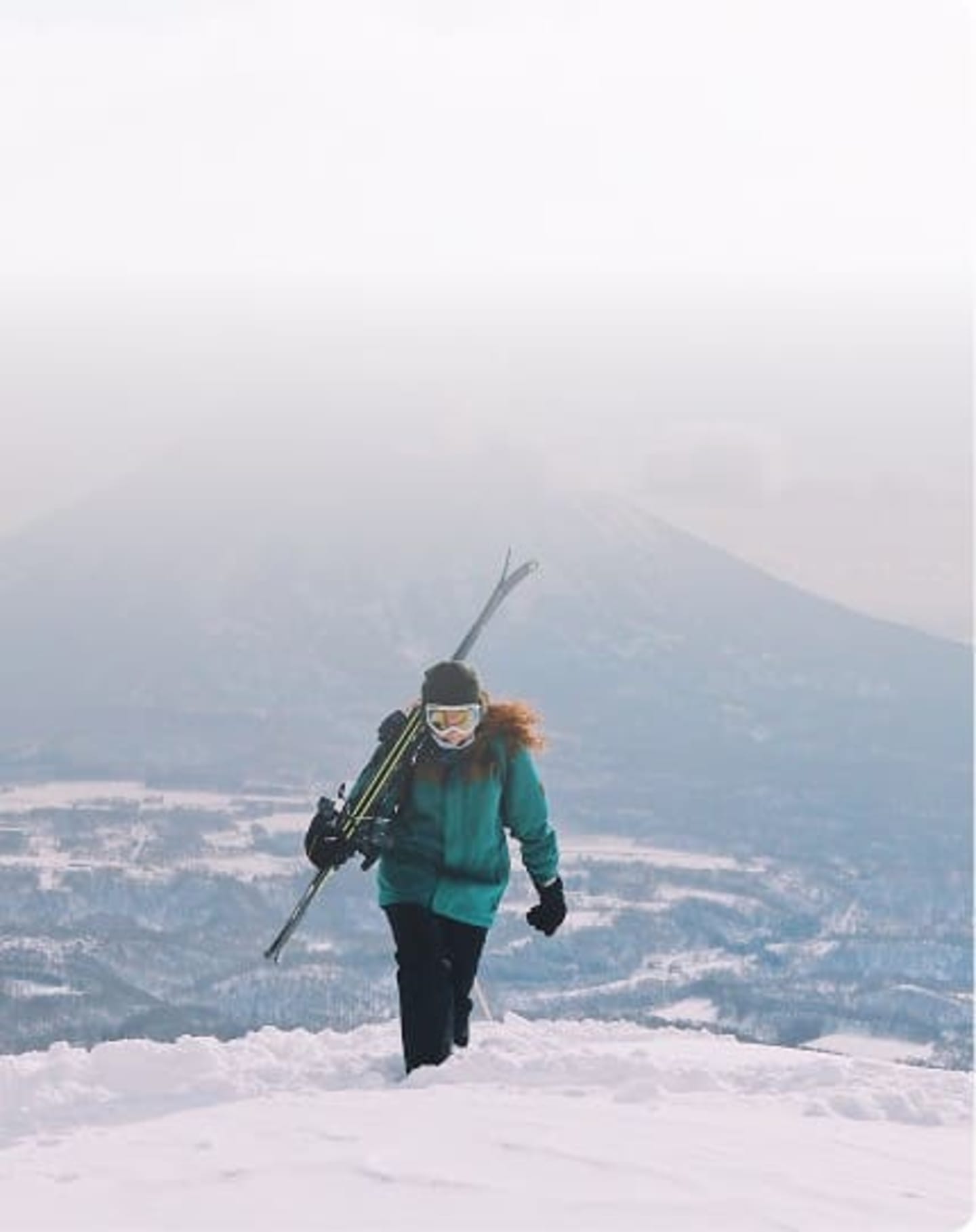 Skier walking with skis over shoulder on a foggy mountain slope in Niseko, Japan