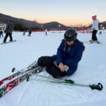 Marnie Adelkopf sitting on the snow beside her skis at sunset