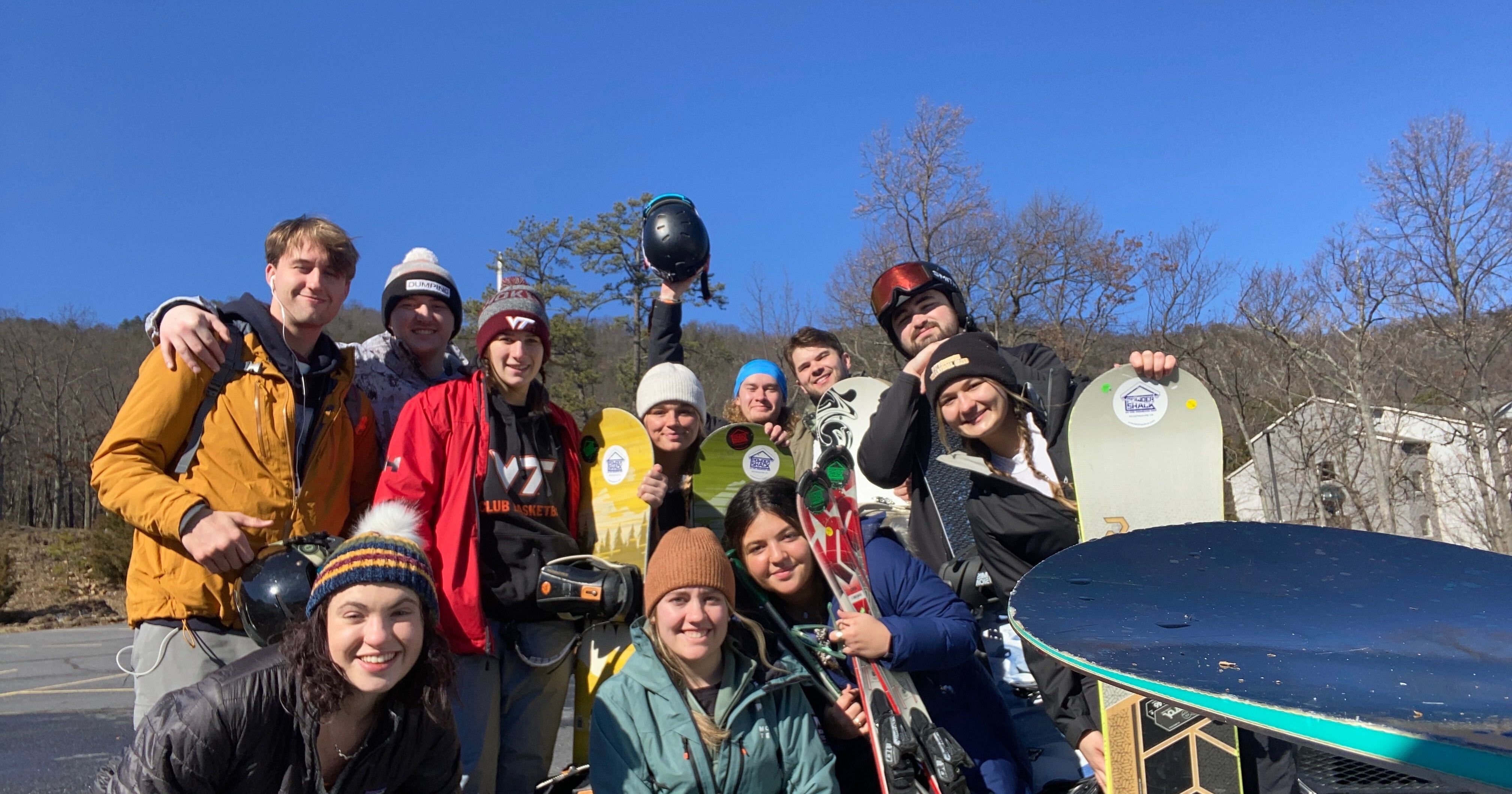 A group of friends posing together with their skis and snowboards in the snow at Snowshoe Mountain under a clear blue sky