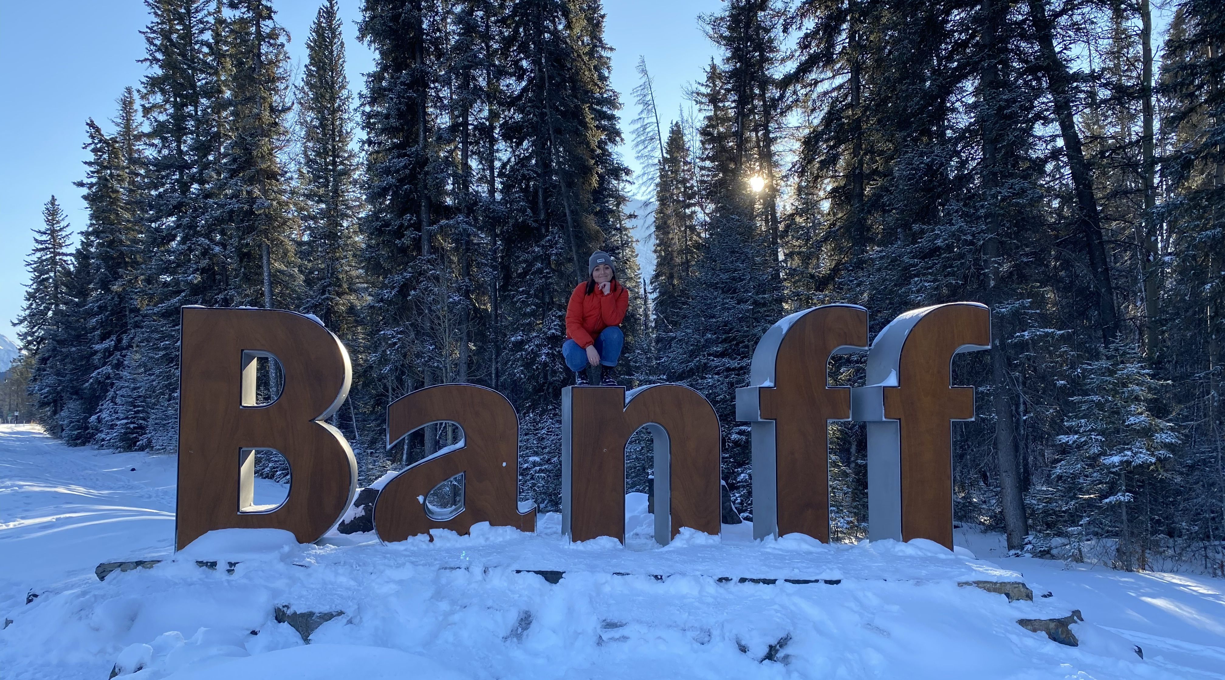 A snowboarder sitting on top of the giant Banff sign, surrounded by snow-covered pines