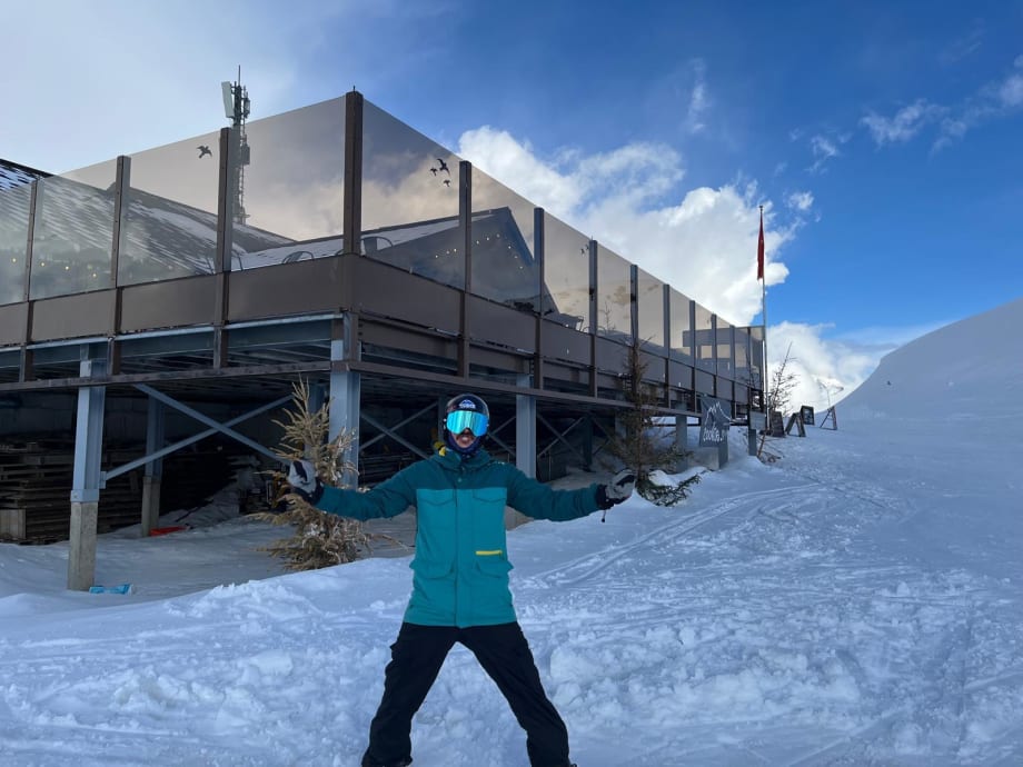 Gibson standing with his arms out in the snow below a glass-fronted mountain building