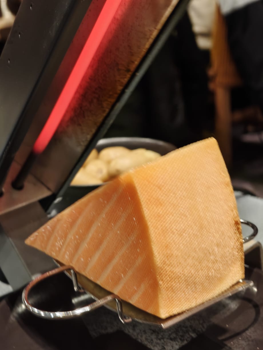 A half wheel of raclette melting under a grill, ready to be scraped onto a plate