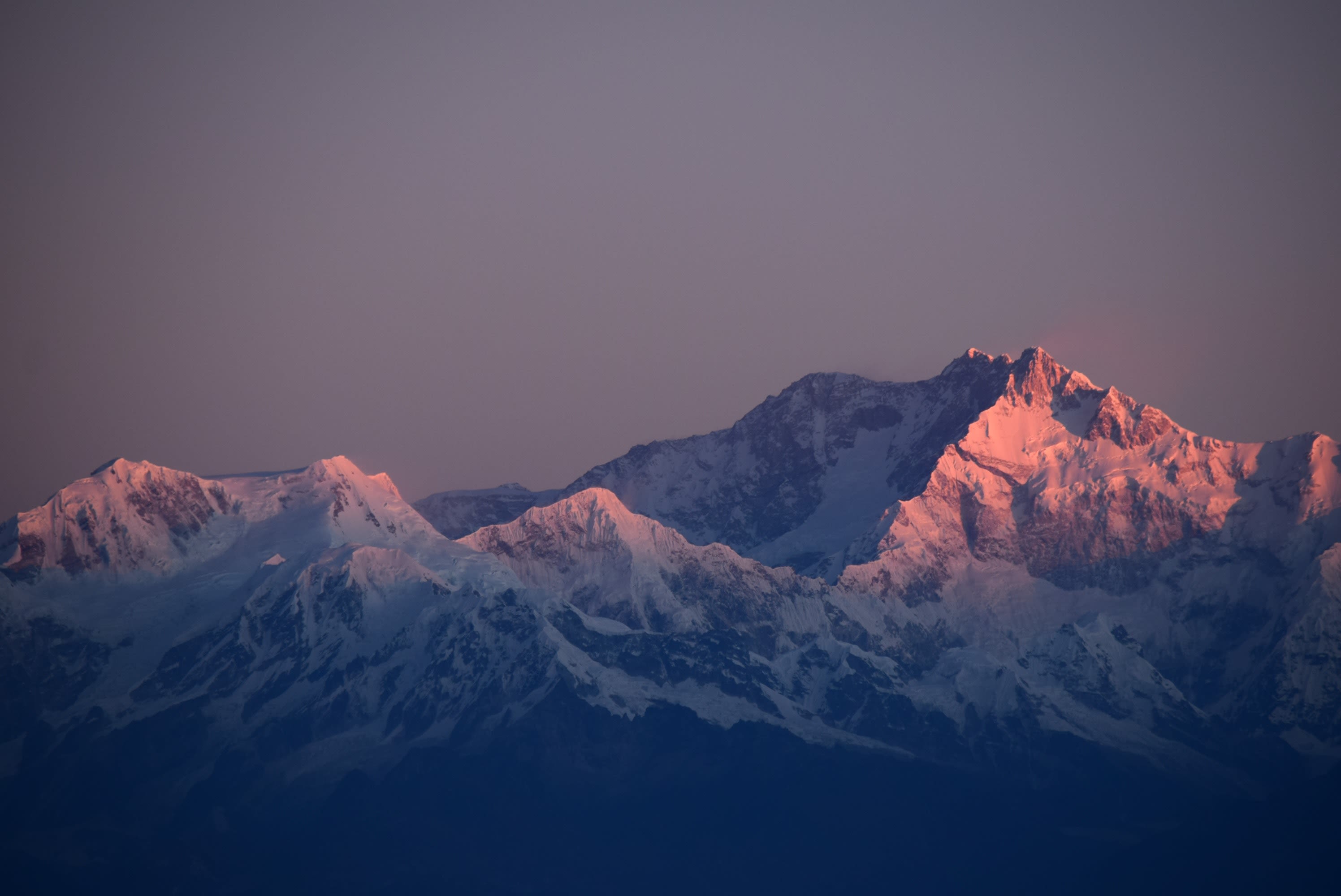 Majestic mountain peaks bathed in a soft pink glow from the rising sun, with snow-covered slopes