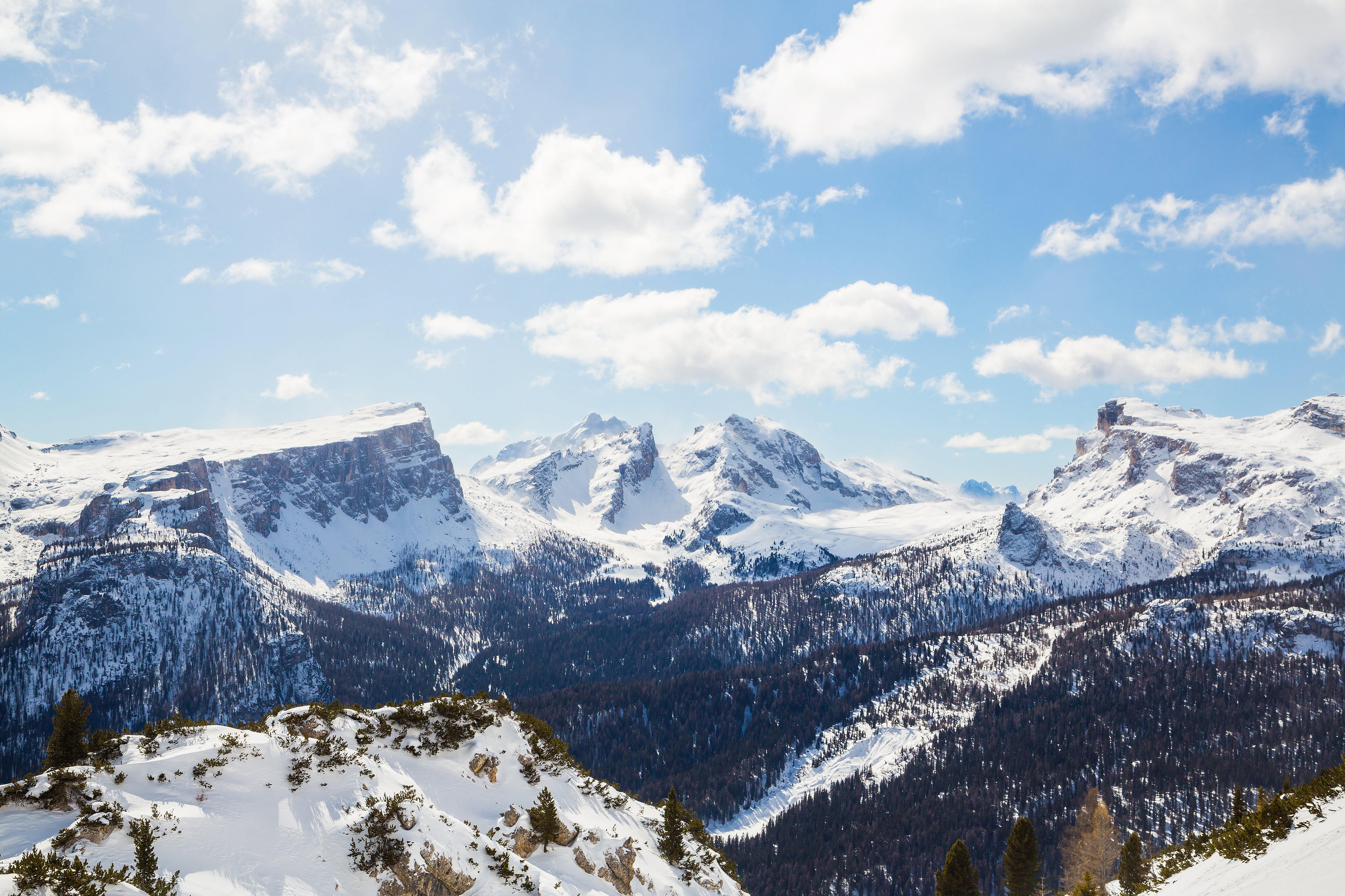 Vast snow-capped mountain range with blue skies and clouds, featuring dramatic ridges and valleys.