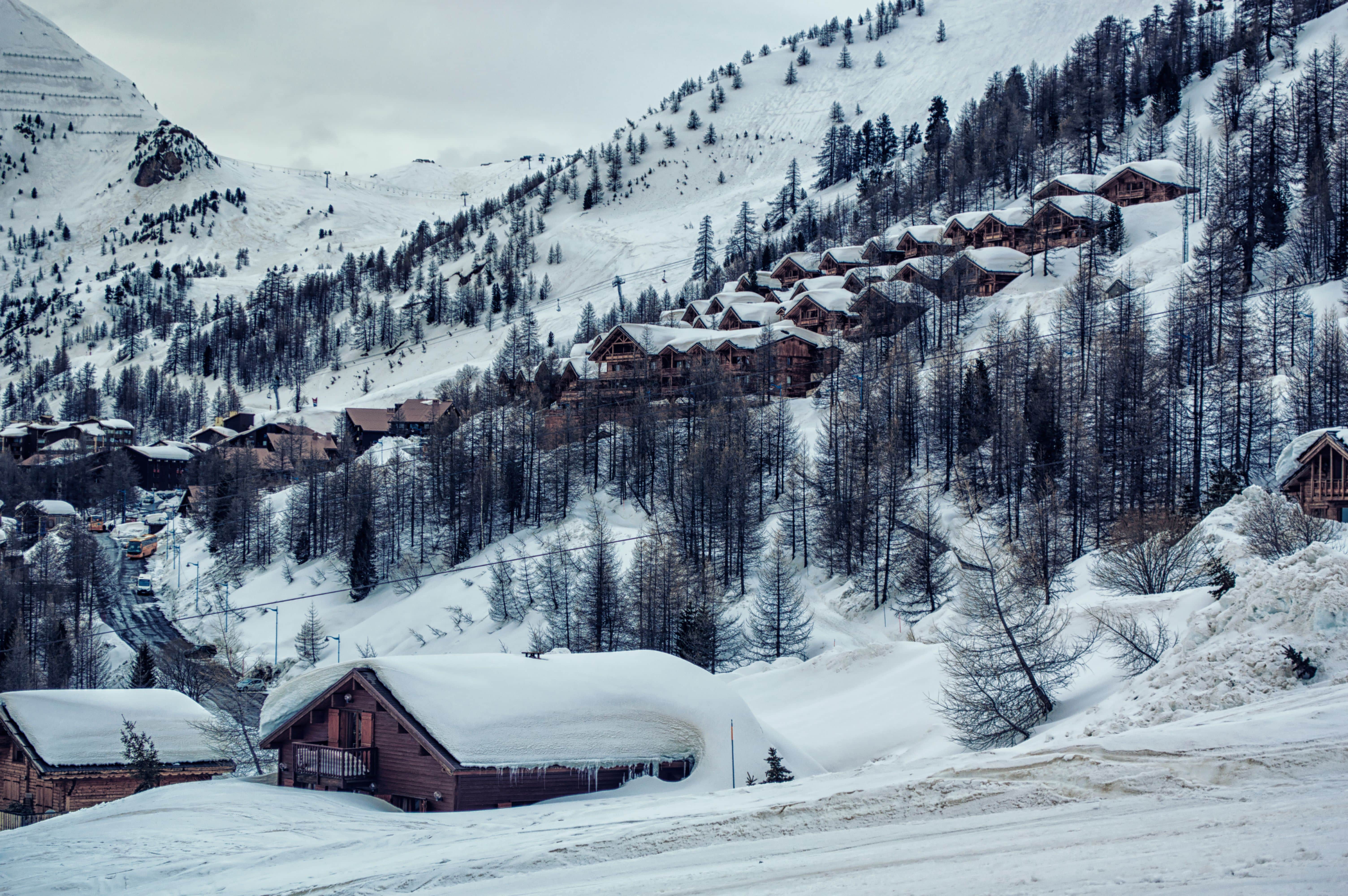 A quaint village nestled at the base of towering snowy peaks under a clear blue sky.