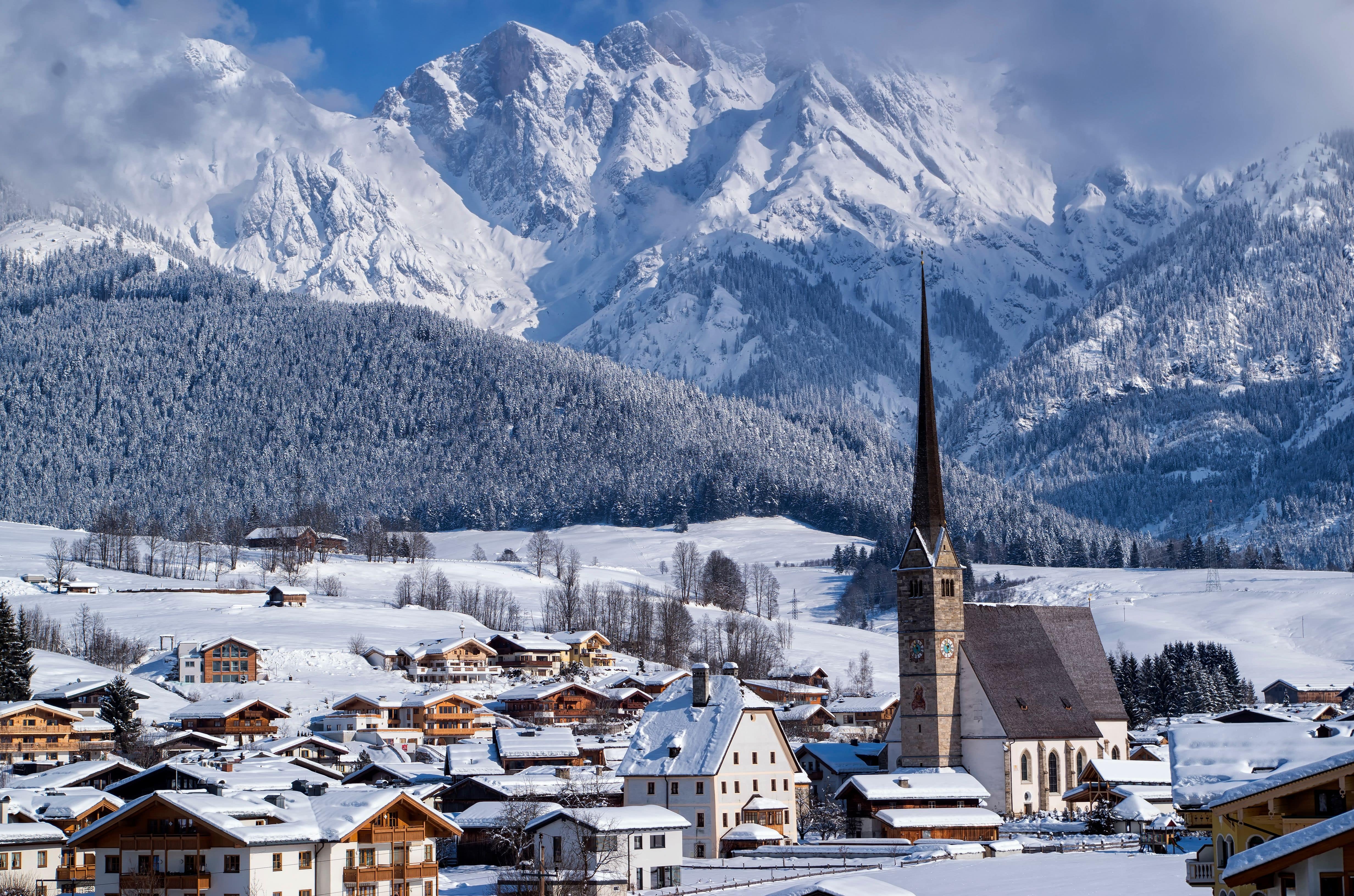 A cluster of chalets on a snow-covered hillside surrounded by trees and ski slopes in the background.