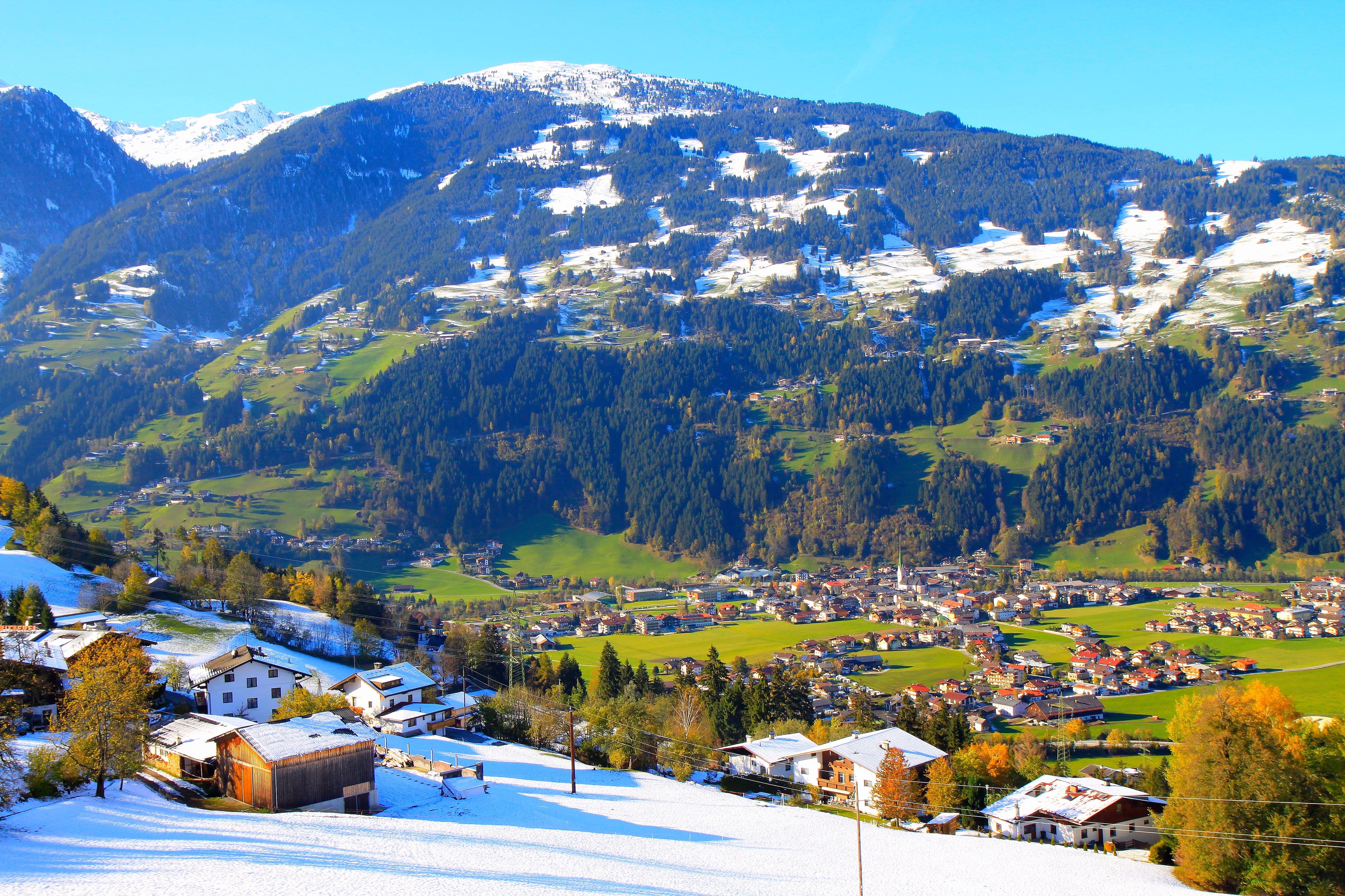 A valley in the early stages of winter, with a village surrounded by mountains and patches of snow