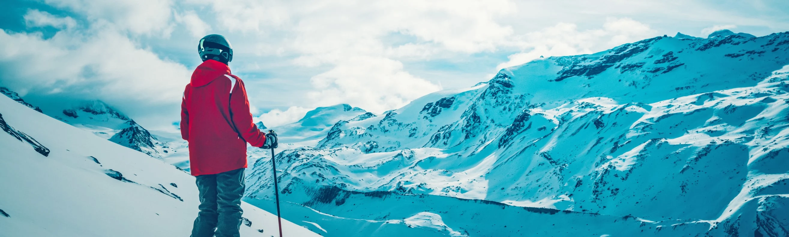 Skier in a red jacket looking at snow-covered mountains in the Swiss Alps on a clear day