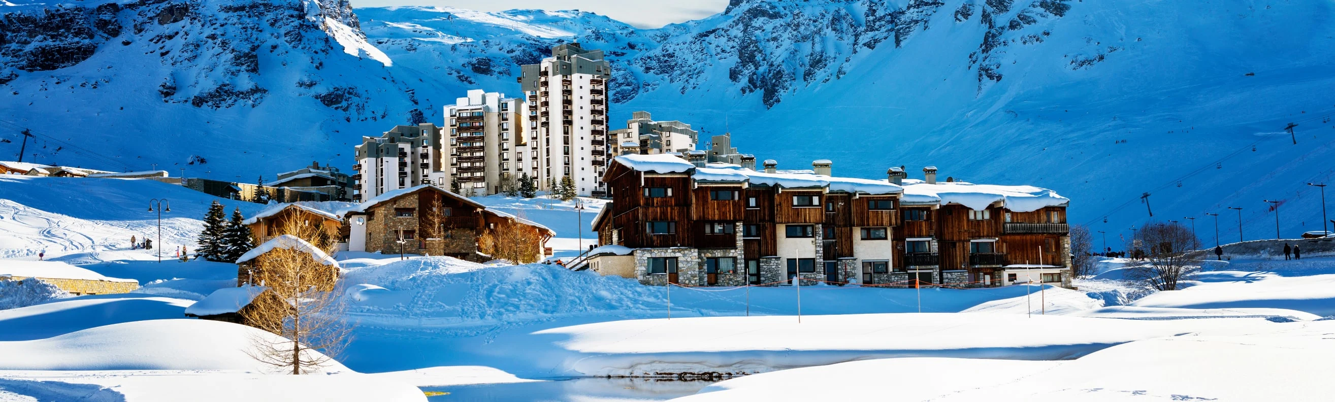 Tignes ski resort with modern and traditional buildings, set against a snowy mountain backdrop, with ski lifts in the distance.