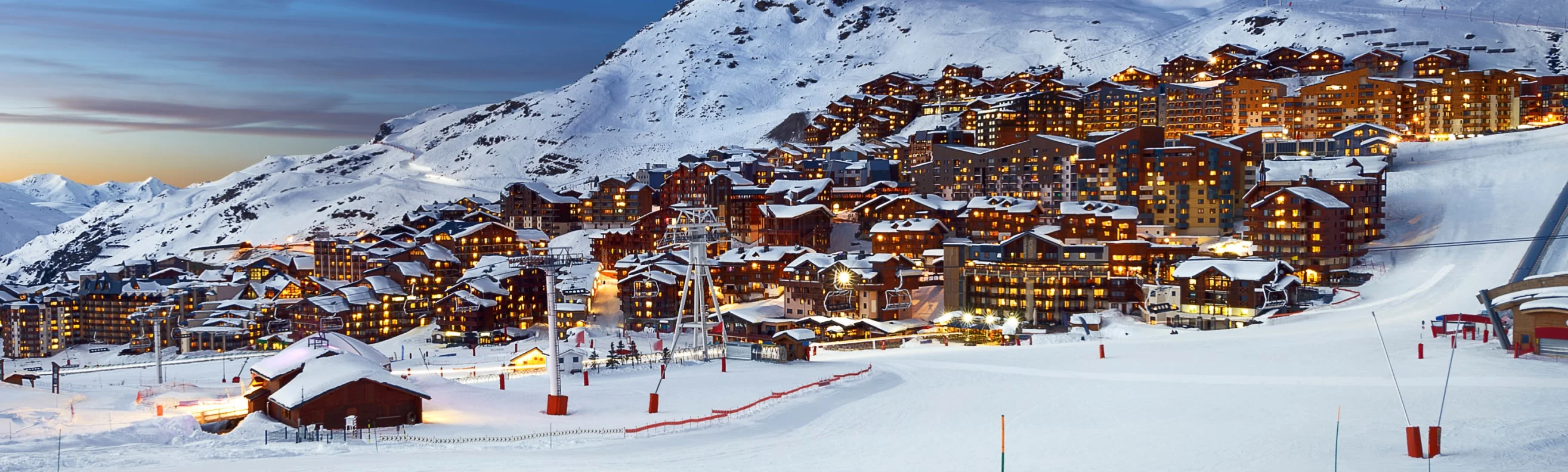 A panoramic view of Val Thorens village at dusk, with buildings lit up against a snowy mountainside.