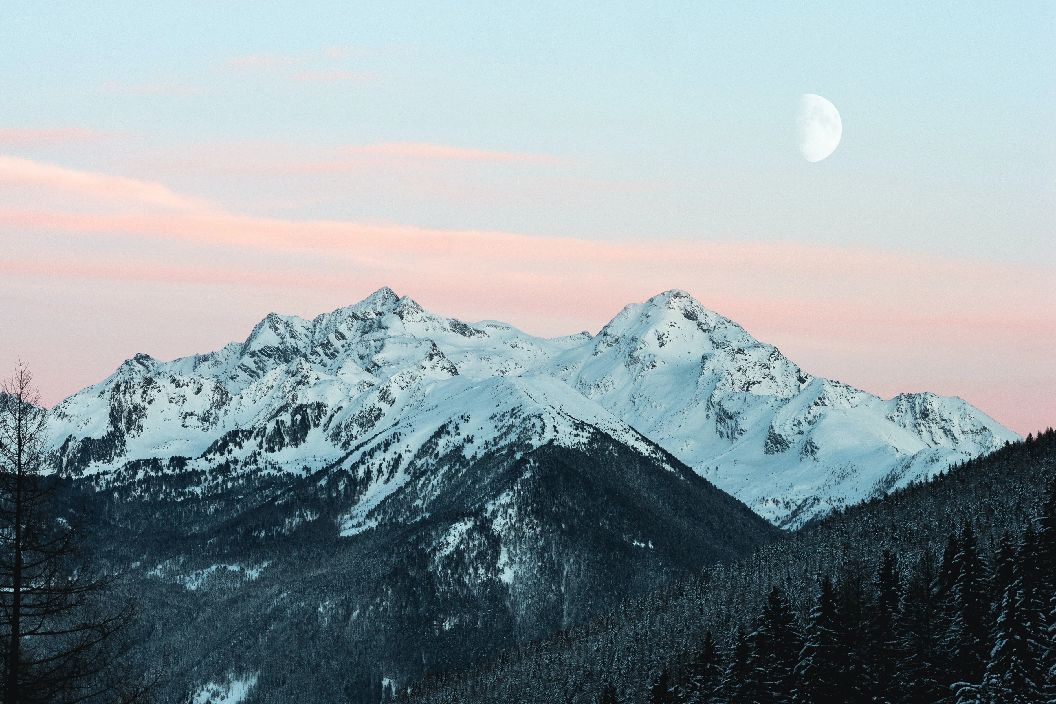 Snow-capped mountain range under a pink-tinted sky with the moon visible in the background.
