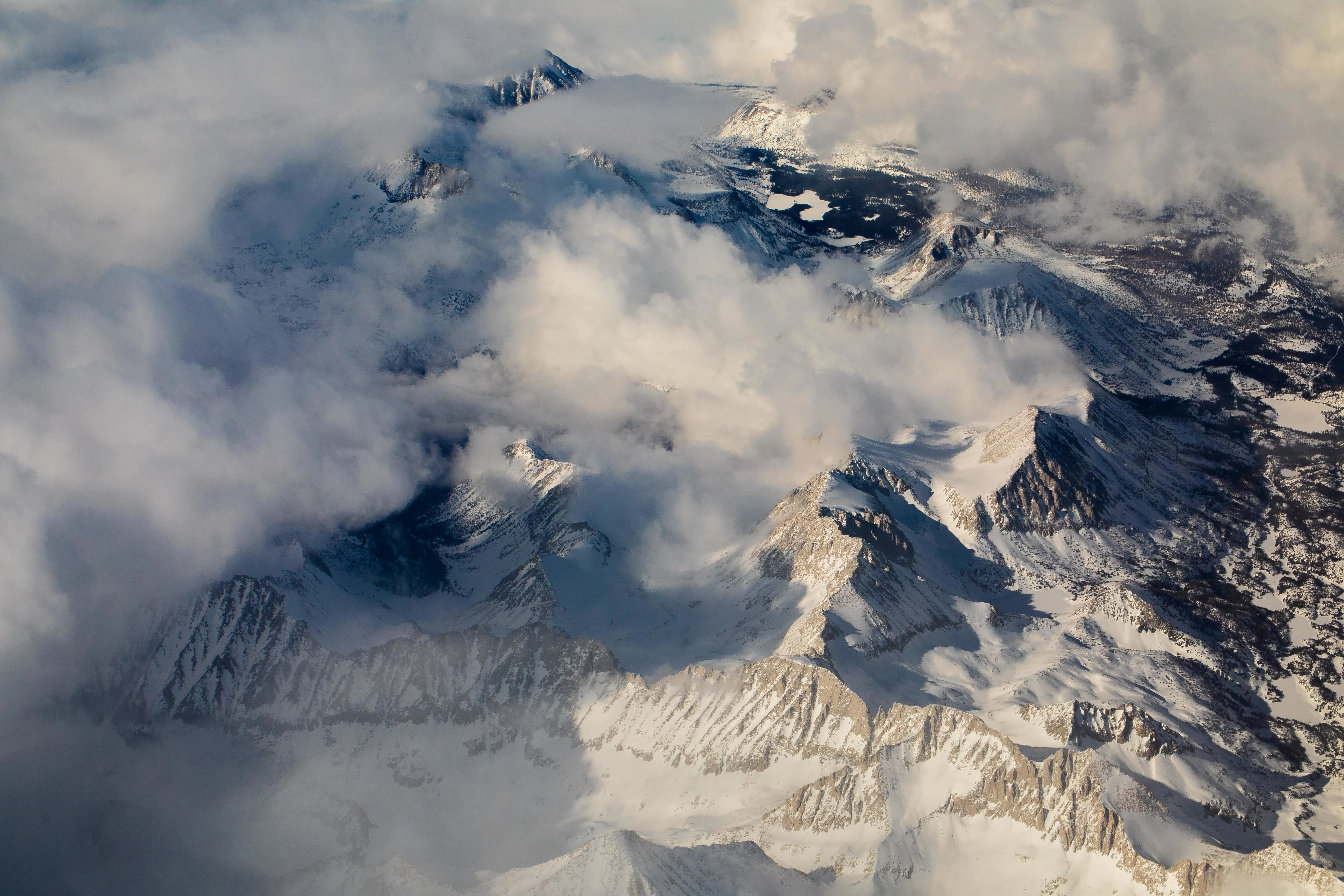 Aerial view of snowy mountain peaks partially covered by clouds.