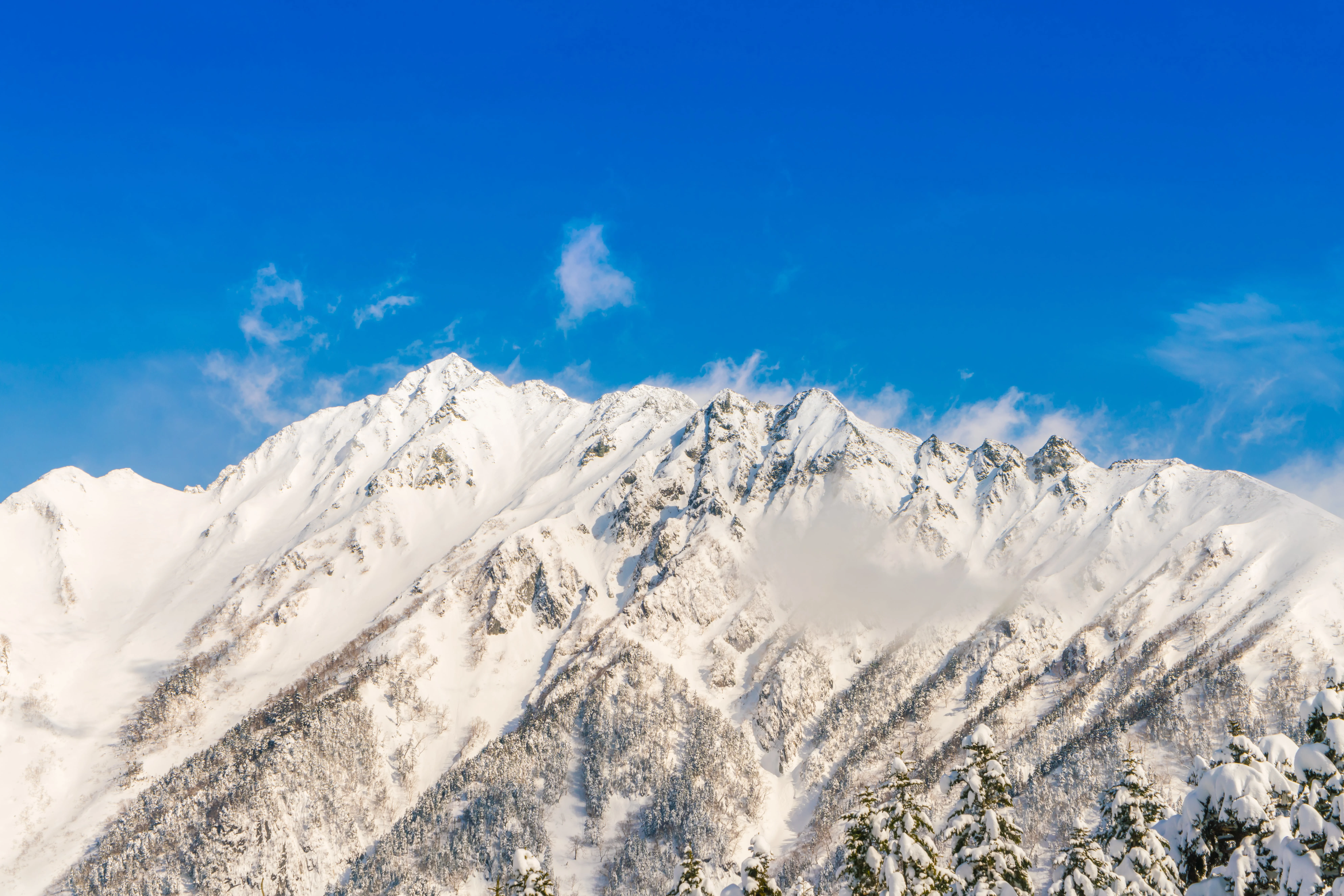 Snow-covered mountain peaks under a bright blue sky with scattered clouds