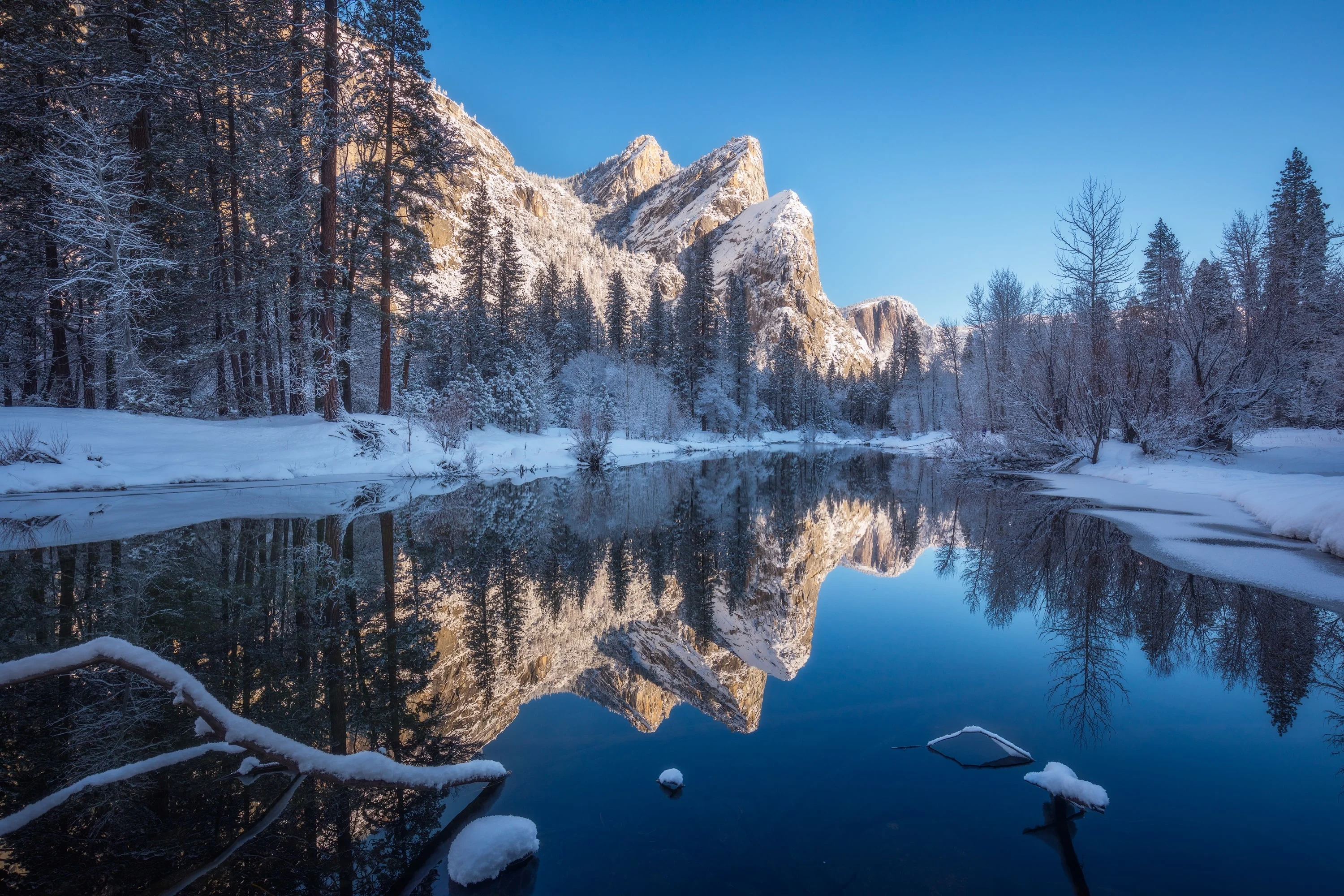 A tranquil, reflective river in a winter forest, with snow-dusted trees and the mountains mirroring in the still water