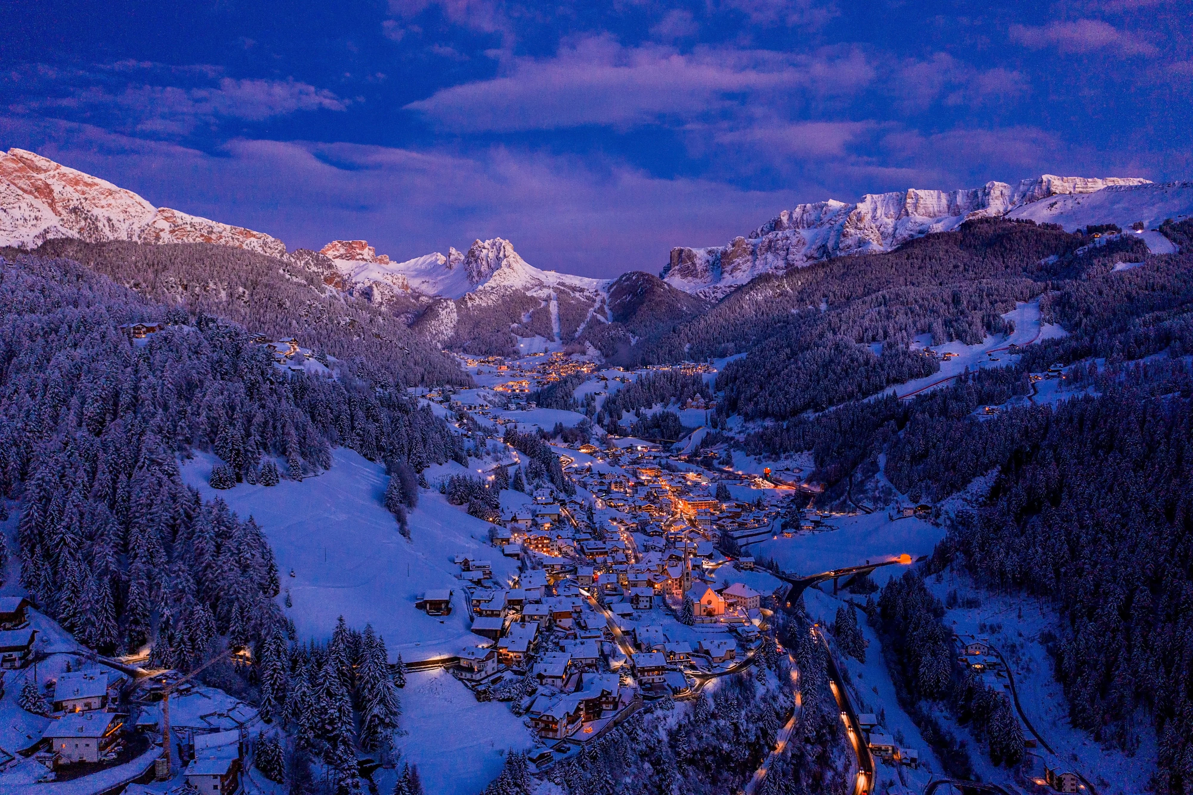 A stunning aerial view of a small village nestled in a valley, surrounded by snow-covered mountains during the evening