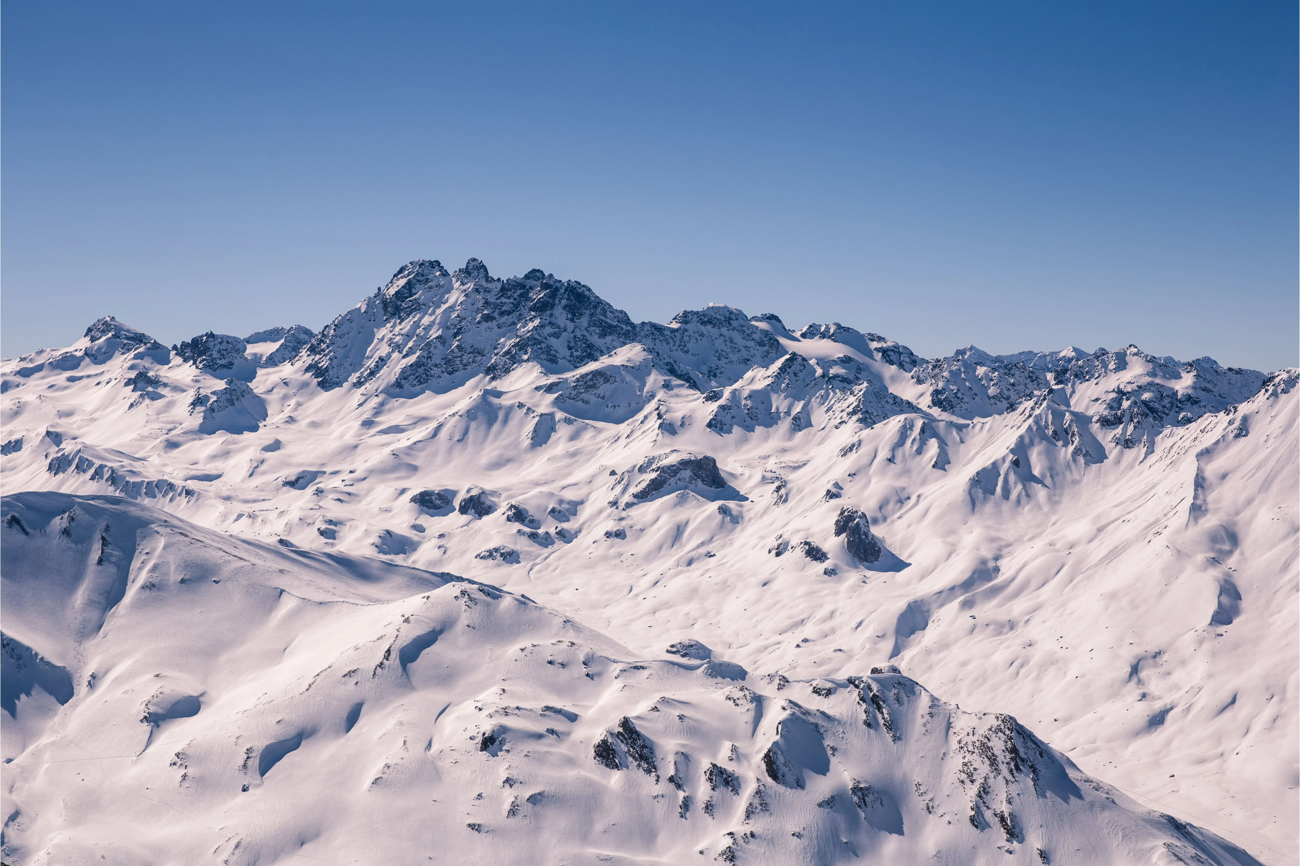 Expansive view of snow-covered mountain peaks under a clear blue sky.