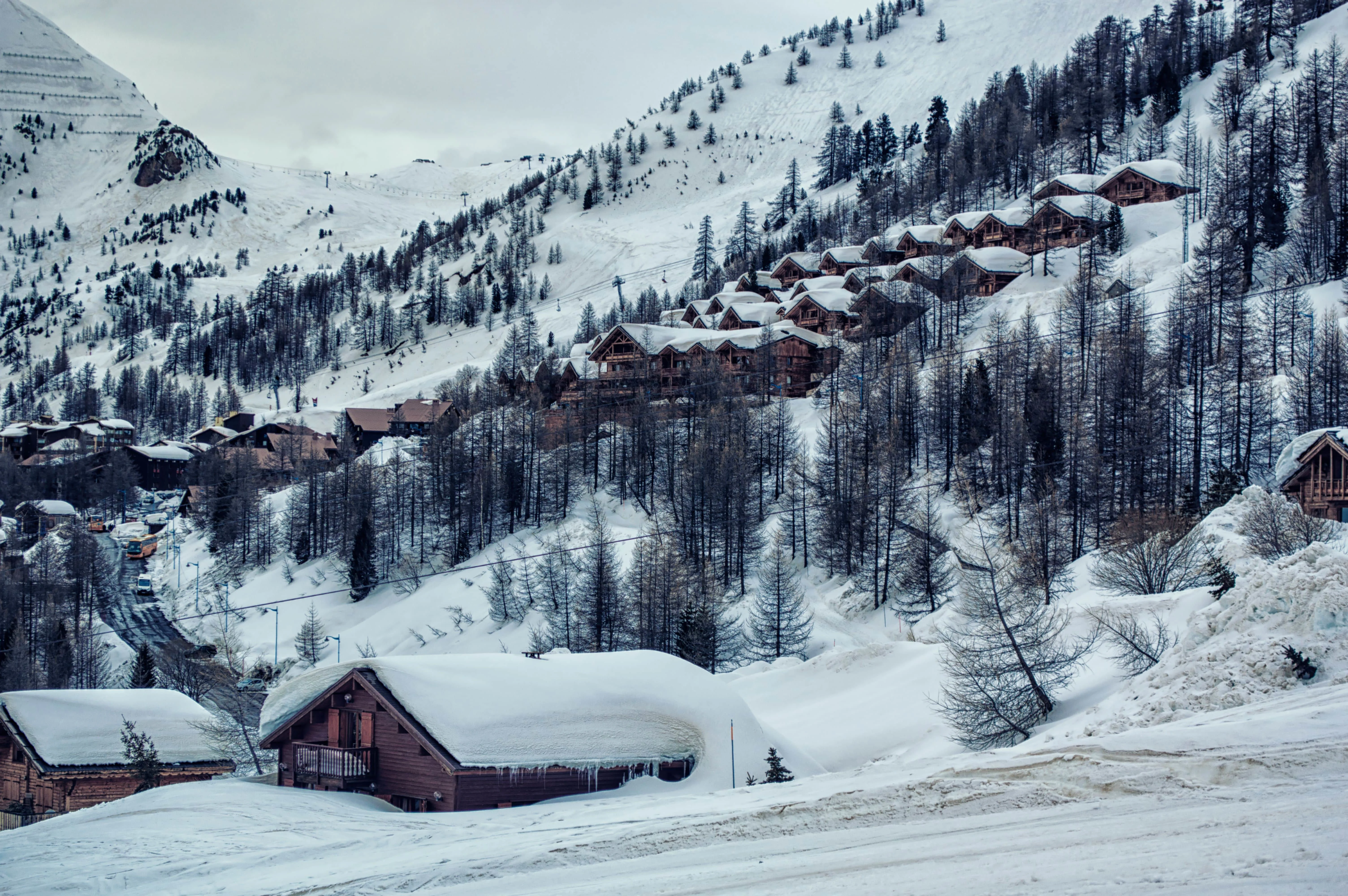 Isola 2000 and its wooden chalets clustered on a snowy hillside, surrounded by snow-covered pine trees and winding ski slopes
