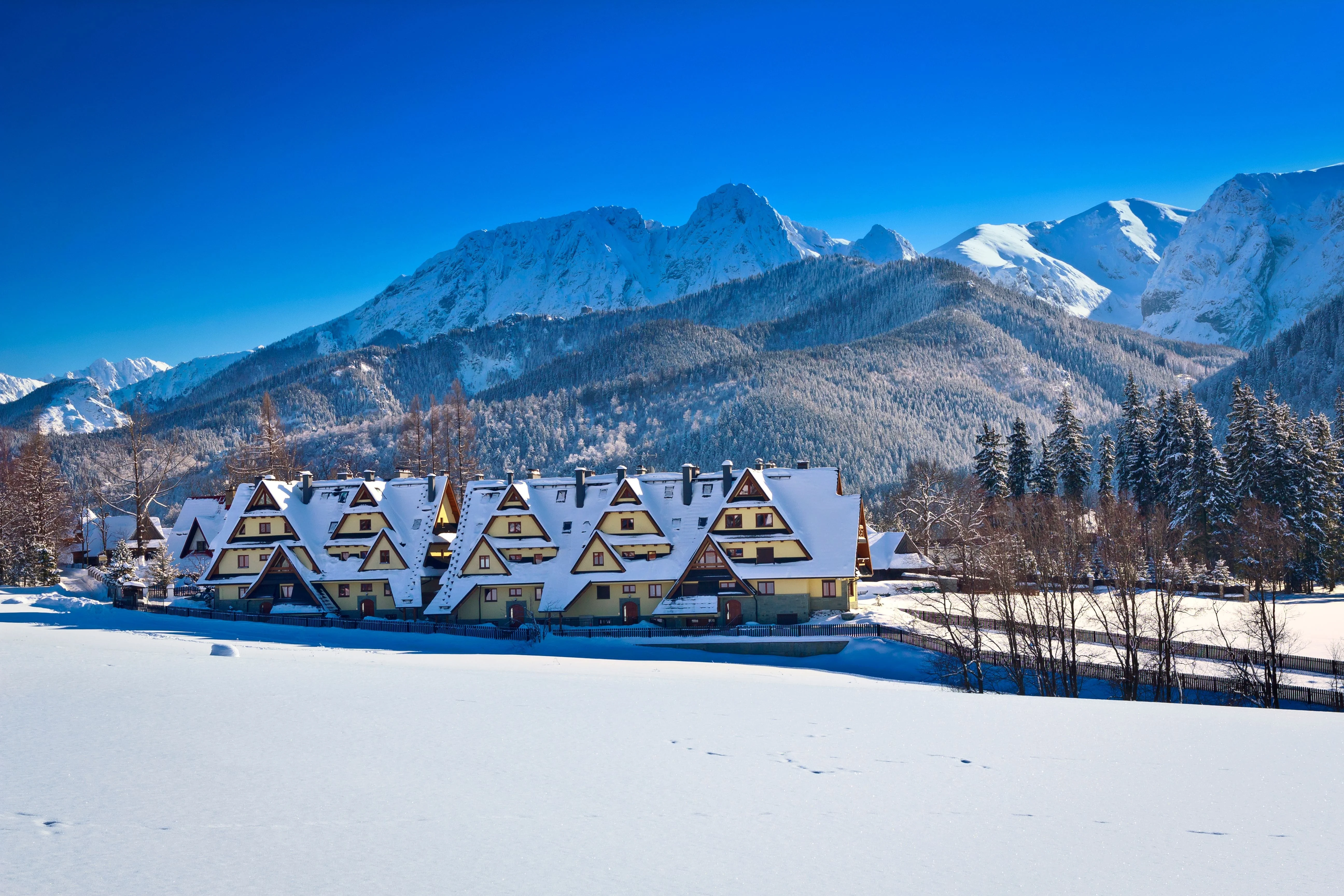 Traditional chalet-style houses covered in snow with a backdrop of the Tatra Mountains in Zakopane
