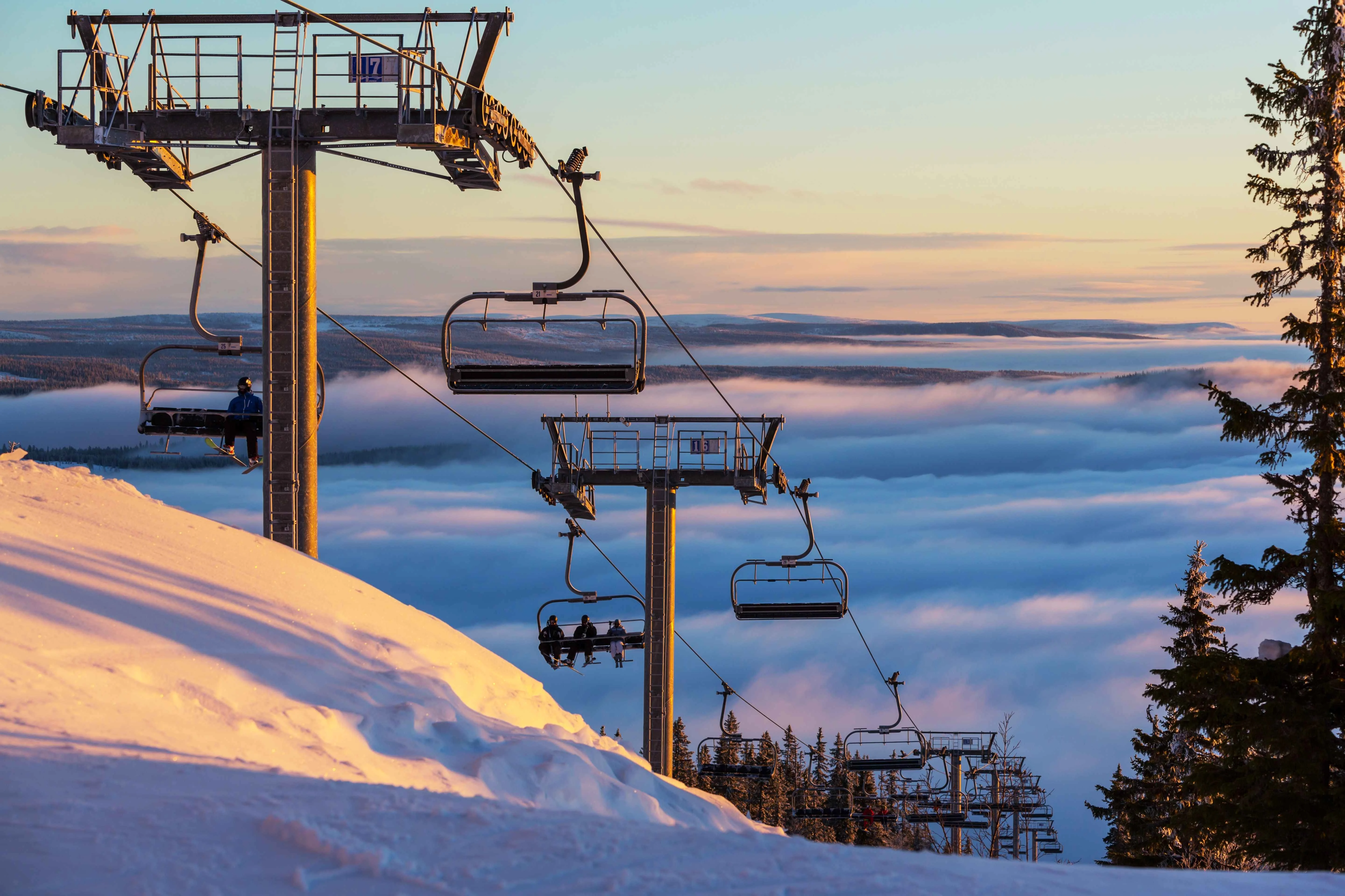 Quad chair lift with people during winter ski season descending through a pine forest covered by clouds