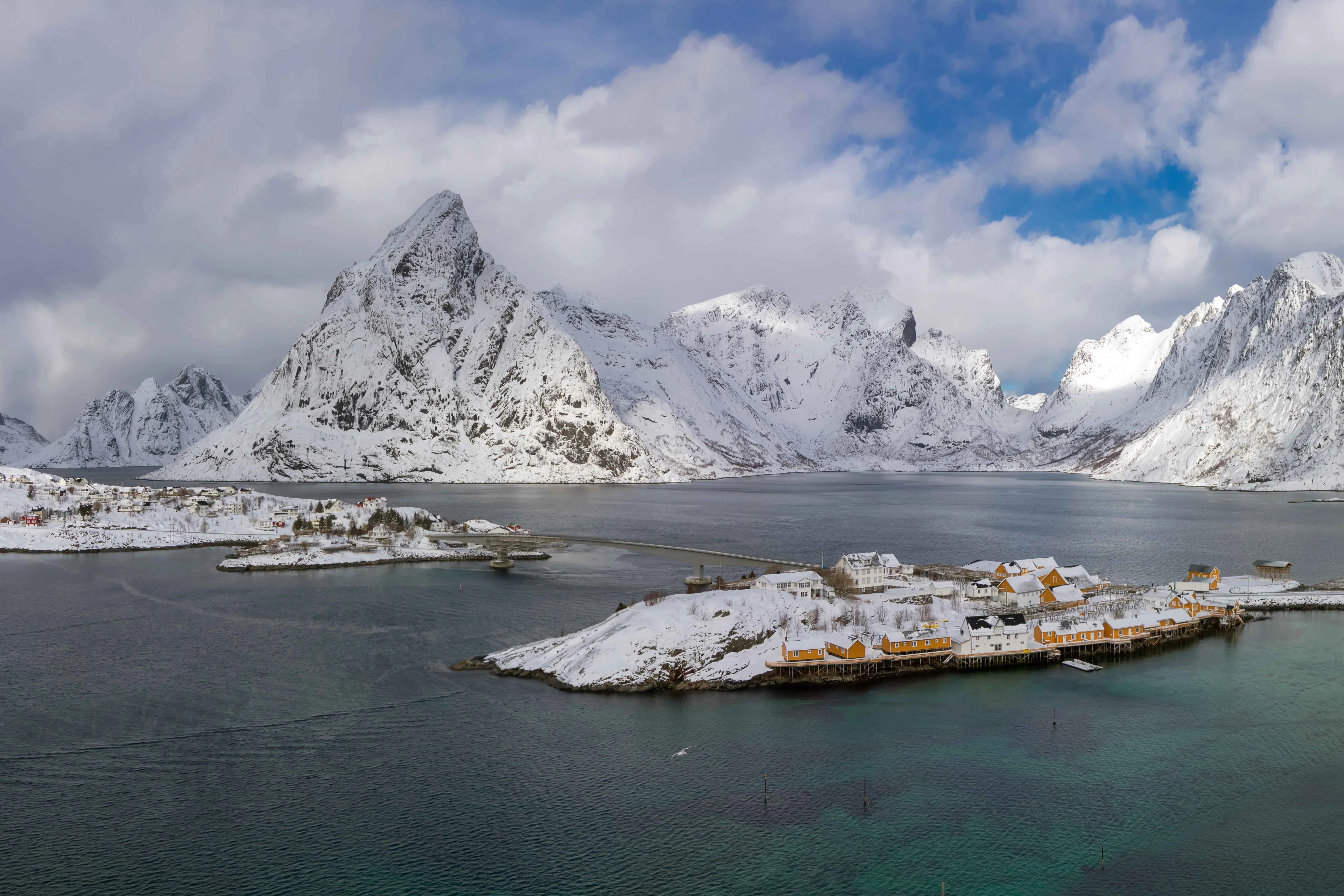 Snow-covered Norwegian fjord landscape with mountains and coastal cabins