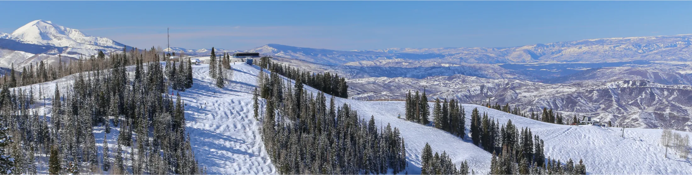 Mountain lodge nestled between snow-covered slopes and pine trees.