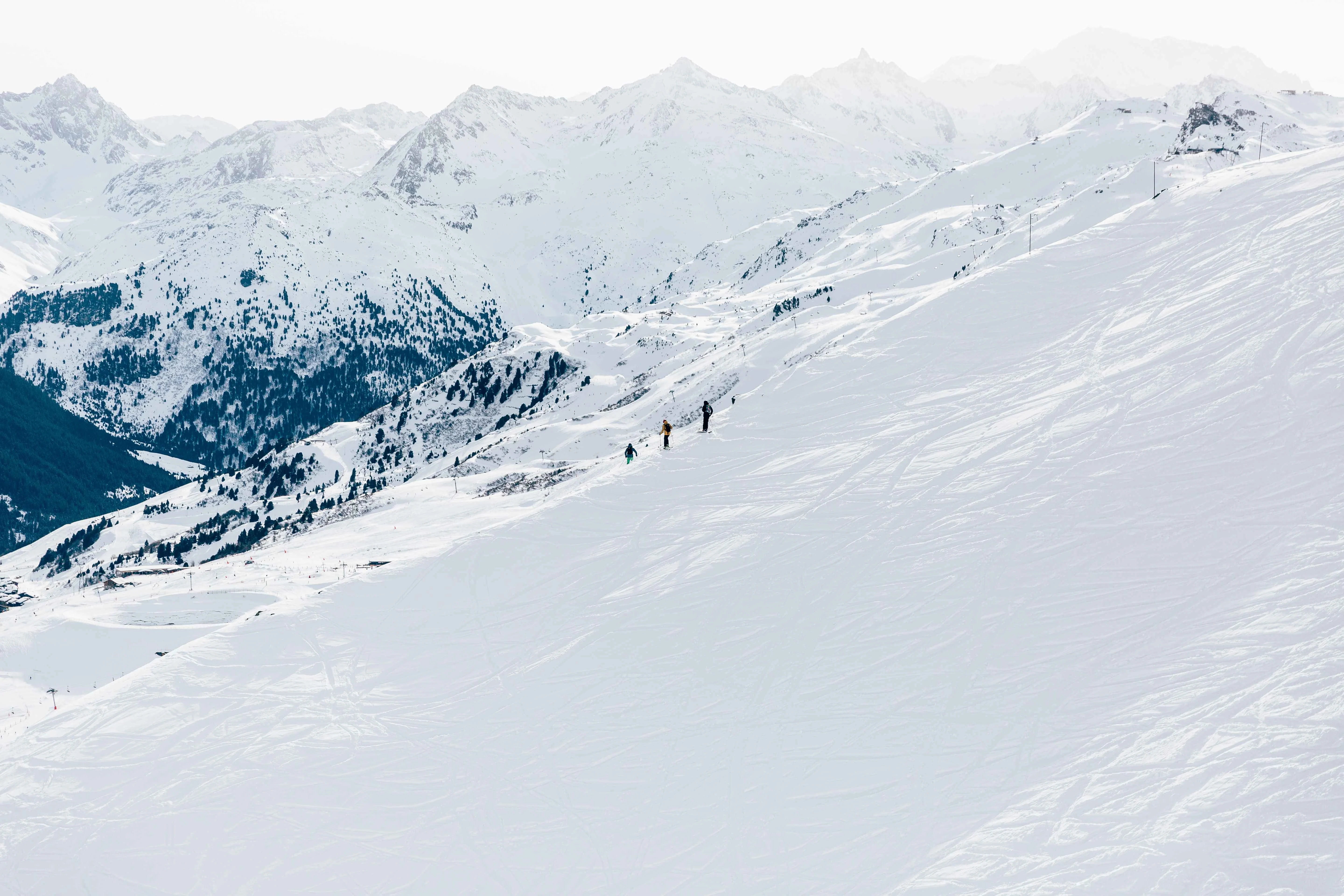 Wide, snow-covered slope in Méribel Centre with a few skiers descending, surrounded by scenic alpine ridges and forested mountain slopes in the background.